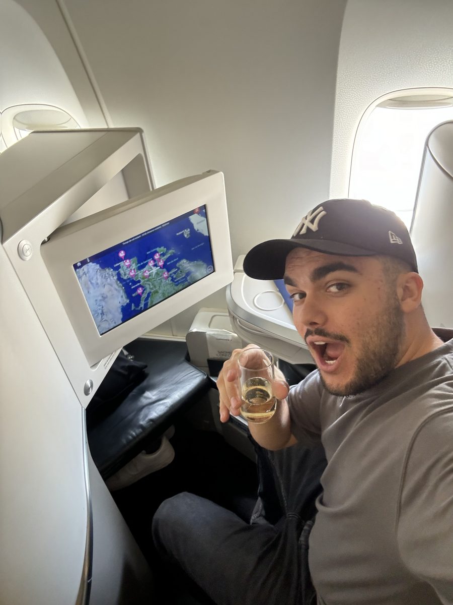 Monsieur Voyage, casquette NY, coupe de champagne à la main dans le siège Best d'Air France, la carte du vol vers Madagascar à l'écran
