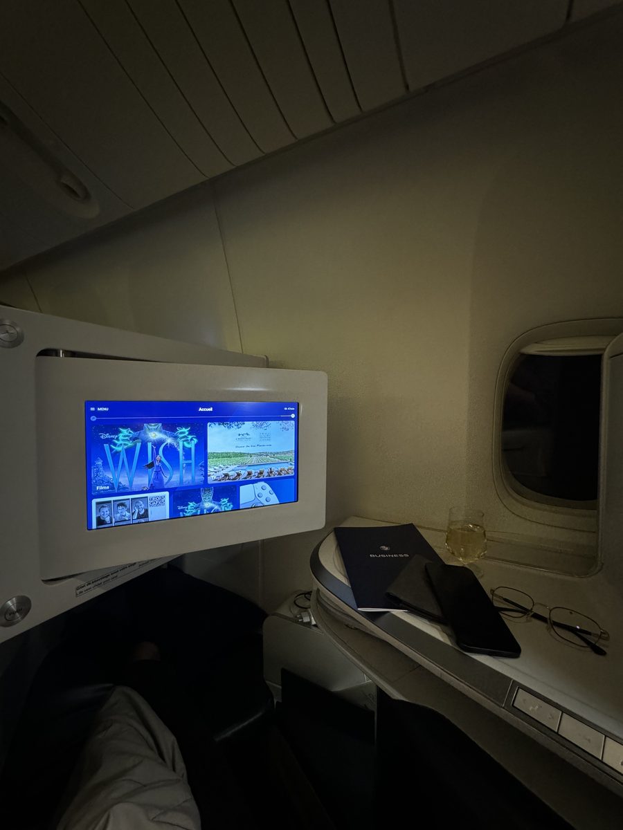 Le menu Business Air France et une coupe de champagne posés sur la tablette du siège Best, écran allumé, avant un vol de nuit