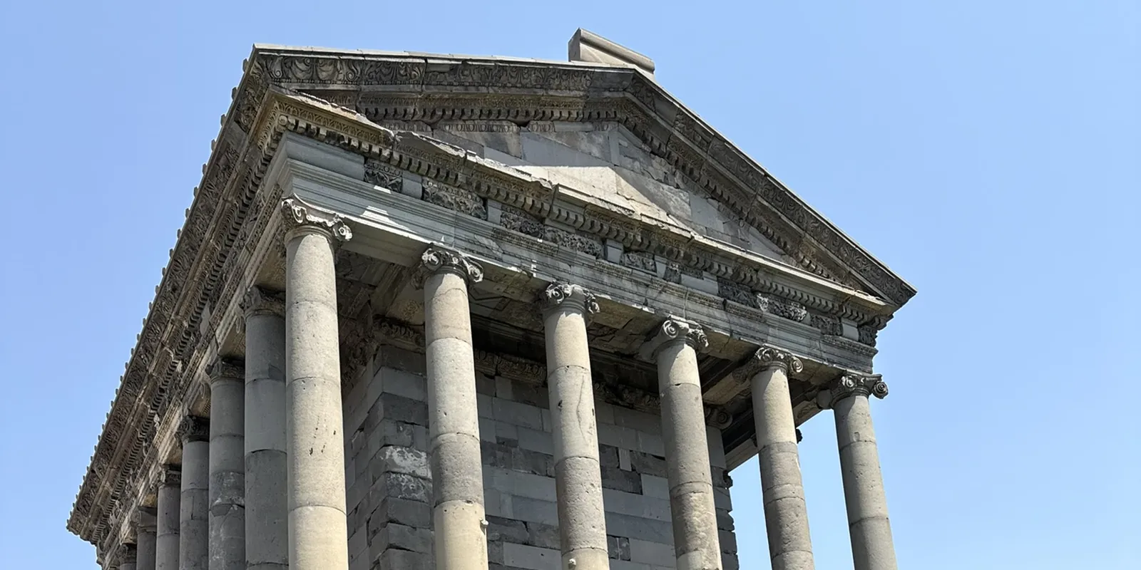 Le temple gréco-romain de Garni vu en contre-plongée : son fronton sculpté et sa colonnade de basalte se détachant sur un ciel bleu sans nuage