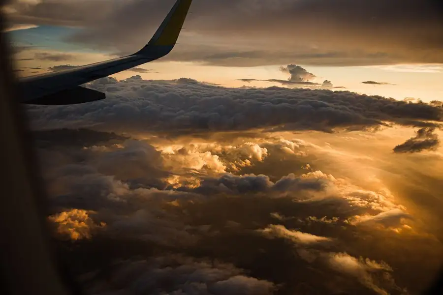 Aile d'avion survolant une mer de nuages dorés au coucher du soleil