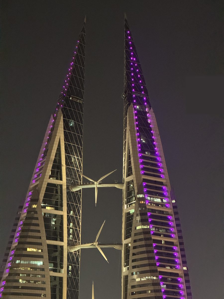 Les deux tours du Bahrain World Trade Center à Manama illuminées en violet la nuit, avec leurs trois éoliennes suspendues