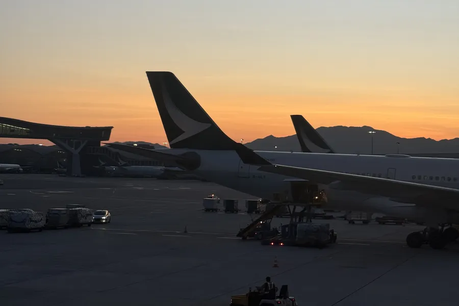 Dérives d'avions Cathay Pacific sur le tarmac de l'aéroport de Hong Kong au coucher du soleil, montagnes en arrière-plan