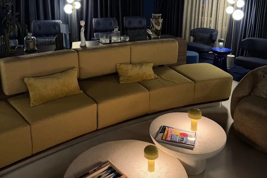 Canapé courbe moutarde, lampes à globes et fauteuils bleu nuit dans le salon Business Corsair de l'aéroport de La Réunion