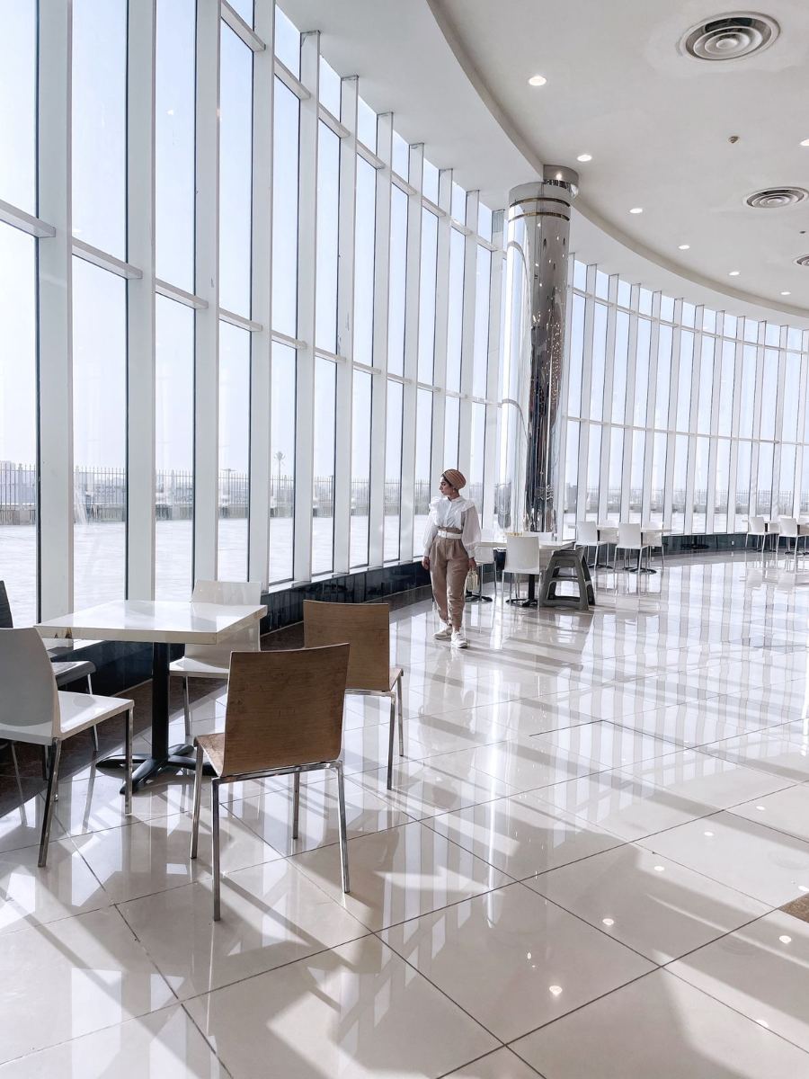 Tables et chaises devant une immense baie vitrée, dans un salon d'aéroport au sol de marbre très lumineux