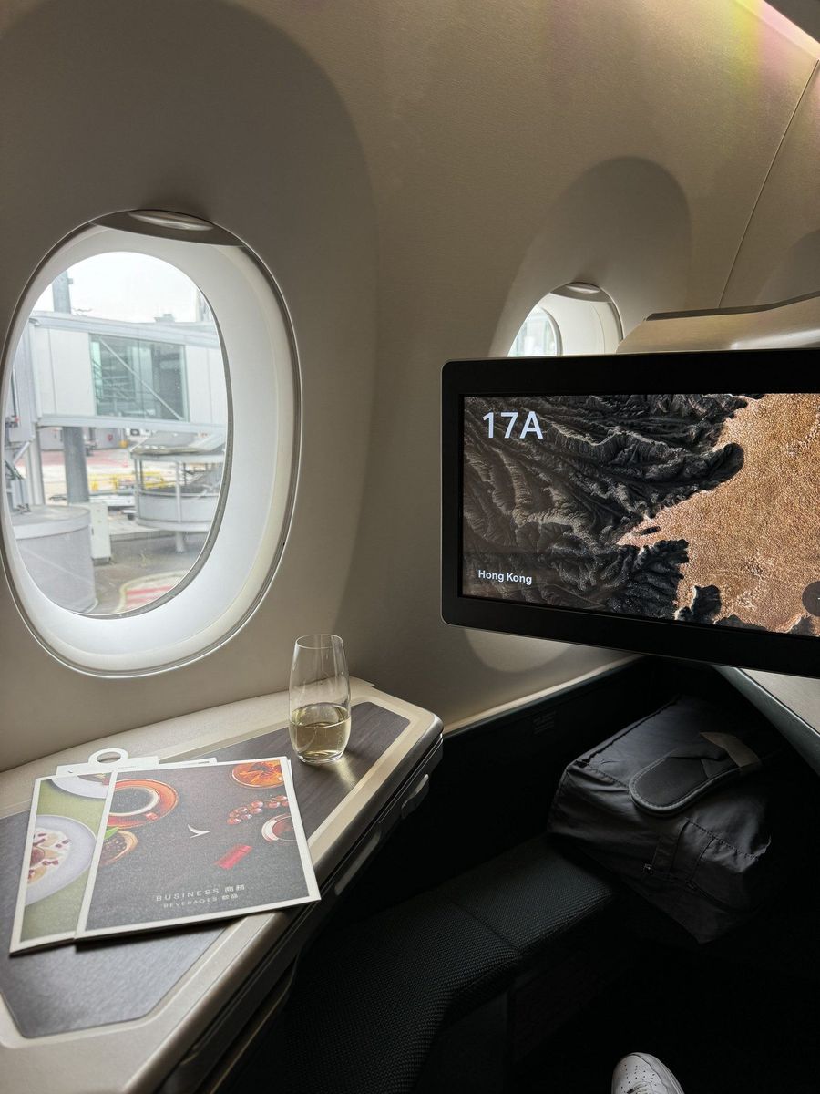 Siège 17A de la classe affaires Cathay Pacific avec verre de bienvenue et cartes de menu sur la tablette, écran individuel affichant une vue aérienne de Hong Kong