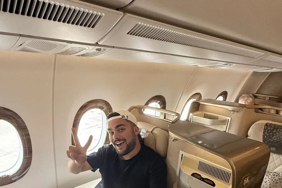 Moi, casquette à l'envers, faisant le V de la victoire depuis le siège 6K de la classe affaires Emirates sur l'A350, hublots ouverts sur le tarmac