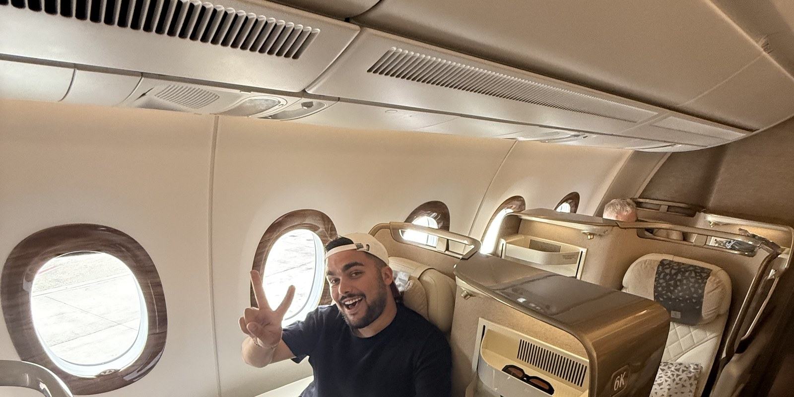 Moi, casquette à l'envers, faisant le V de la victoire depuis le siège 6K de la classe affaires Emirates sur l'A350, hublots ouverts sur le tarmac