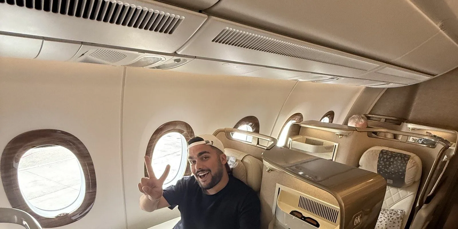 Moi, casquette à l'envers, faisant le V de la victoire depuis le siège 6K de la classe affaires Emirates sur l'A350, hublots ouverts sur le tarmac