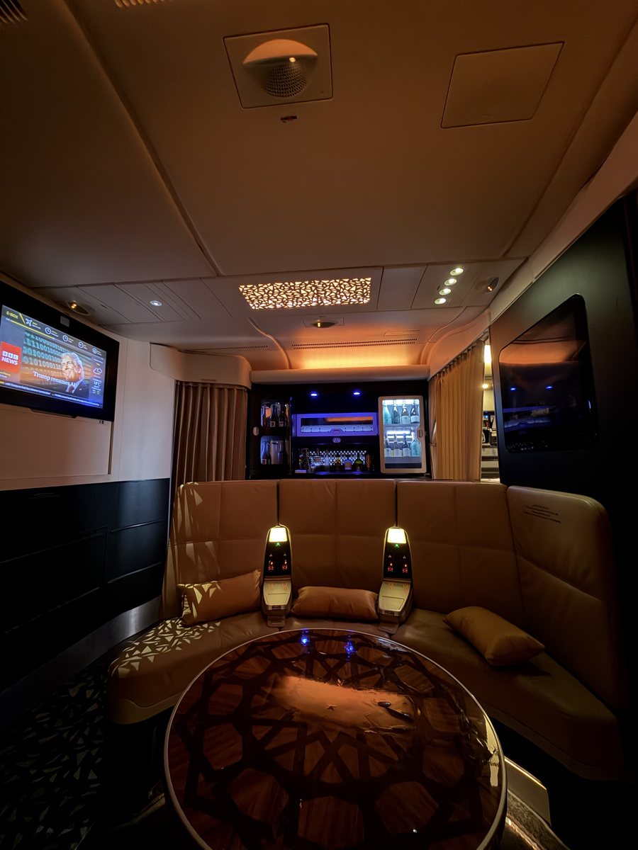 The Lobby de l'A380 d'Etihad : banquette en cuir beige en demi-cercle autour d'une table ronde, bar éclairé avec bouteilles et vitrine réfrigérée, écran diffusant BBC News