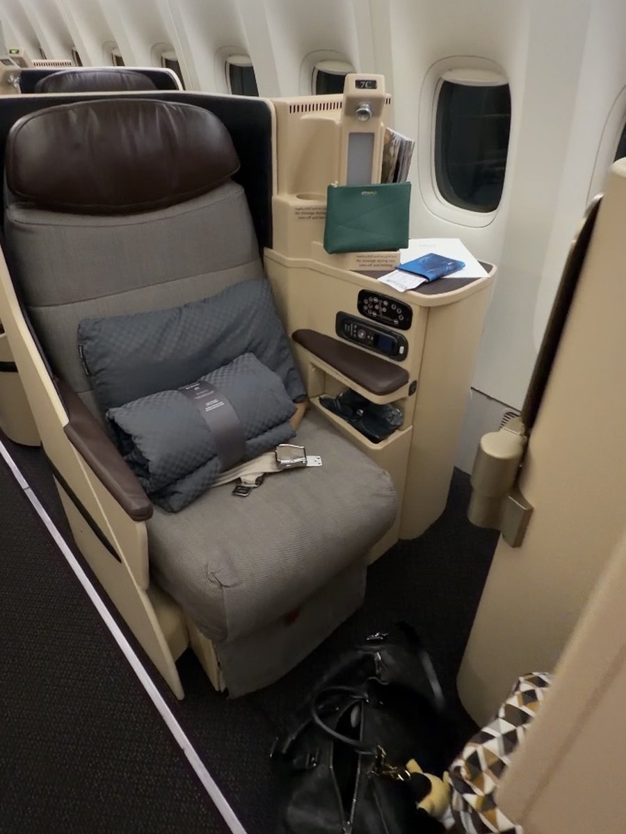 Ancien siège business du Boeing 777-300ER d'Etihad : assise en tissu gris, têtière en cuir marron, coque beige basse, petit écran et trousse LANEIGE verte posée sur la console