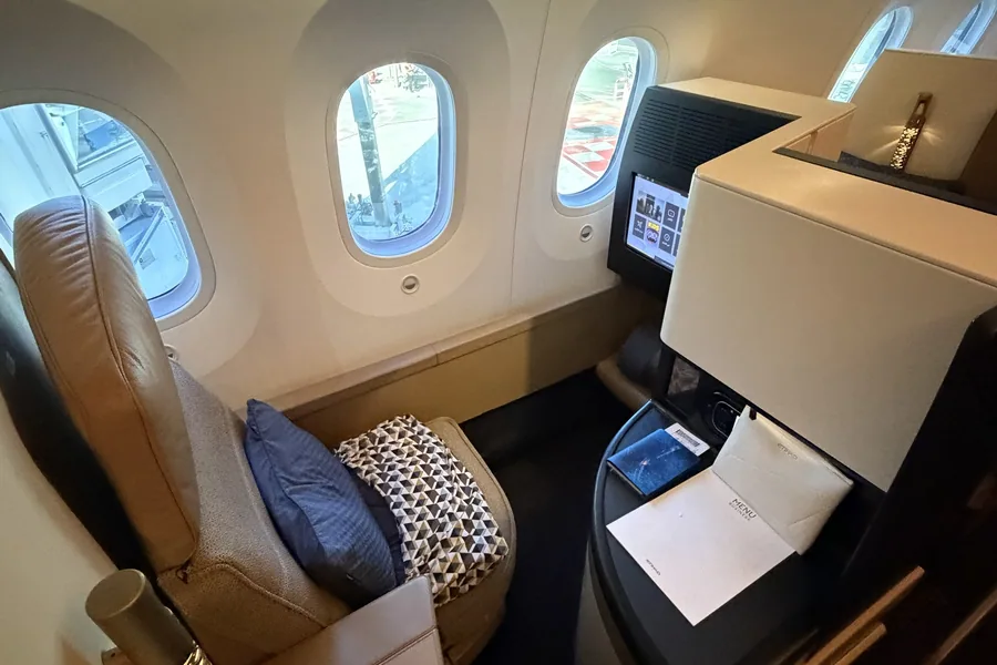 Business Studio du Boeing 787 d'Etihad : siège en cuir camel, grands hublots du Dreamliner, écran allumé et carnet de menu posé sur la console