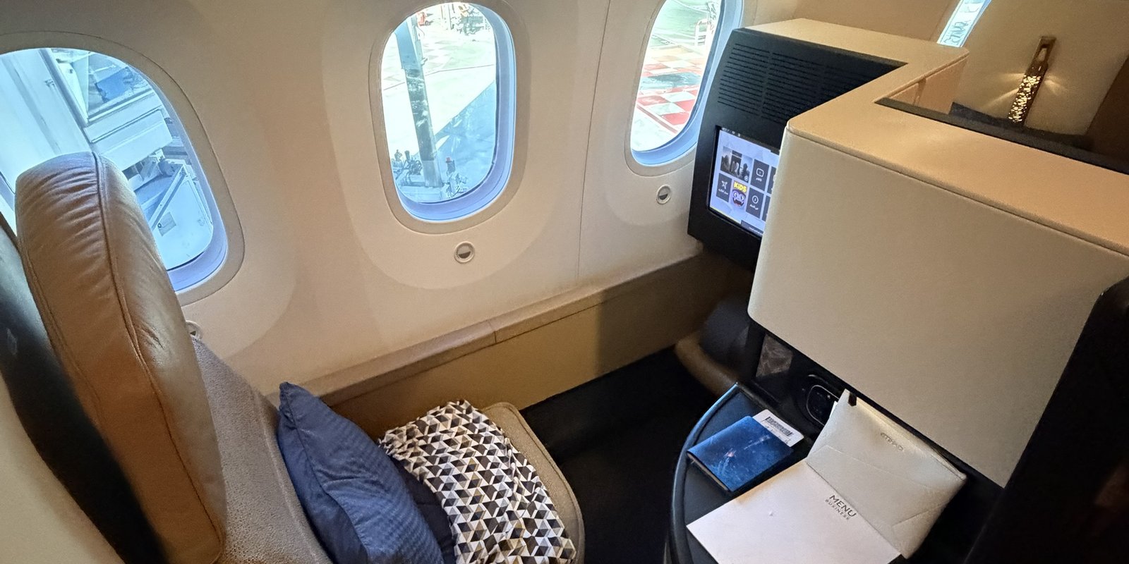 Business Studio du Boeing 787 d'Etihad : siège en cuir camel, grands hublots du Dreamliner, écran allumé et carnet de menu posé sur la console