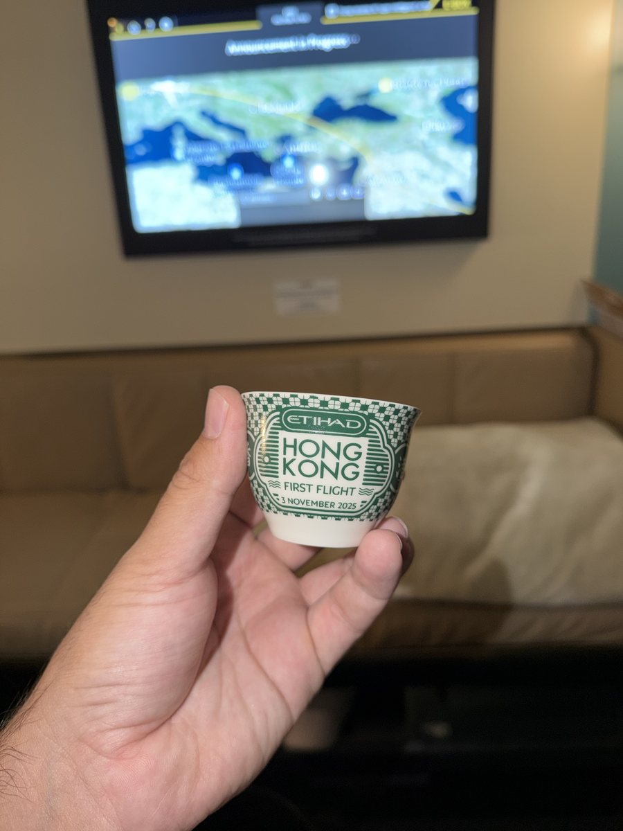Tasse à café arabe finjan d'Etihad, décor vert et blanc, portant l'inscription Hong Kong First Flight 3 November 2025, tenue à la main devant l'écran de la cabine