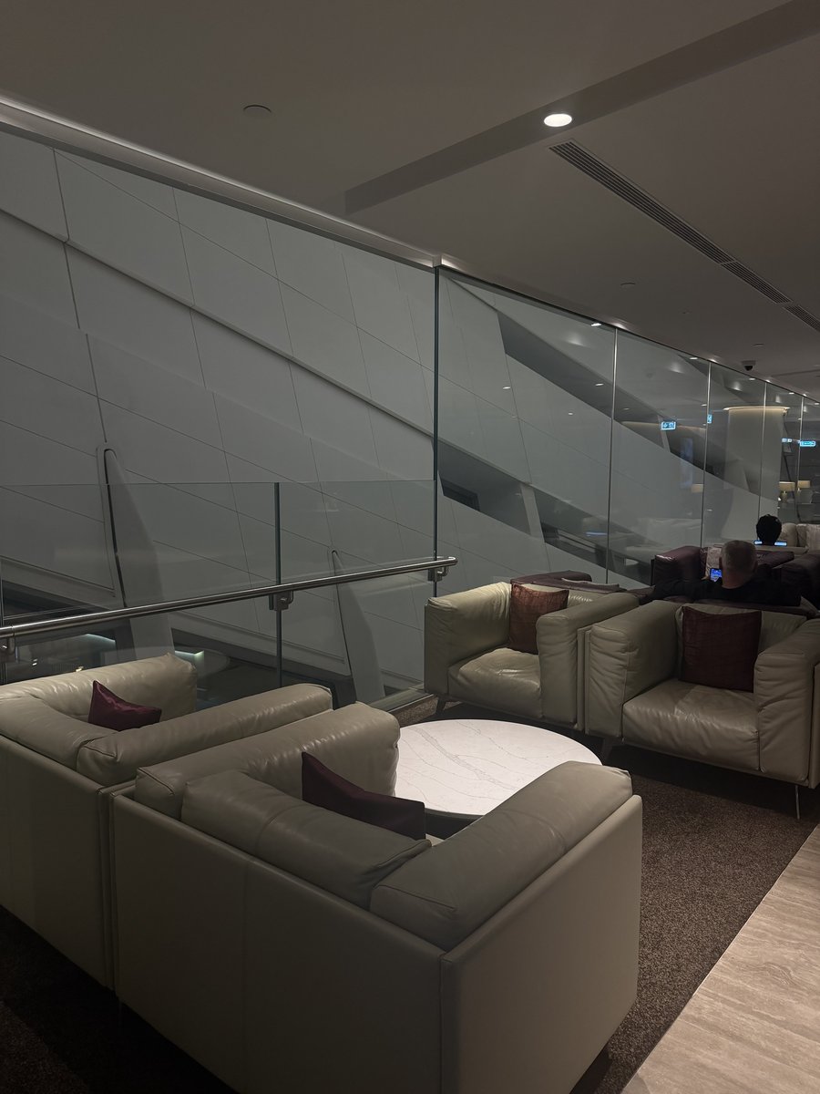 Salon business d'Etihad au Terminal A d'Abu Dhabi : fauteuils et canapés en cuir crème avec coussins bordeaux autour d'une table basse ronde en marbre, le long d'une balustrade vitrée surplombant le niveau inférieur
