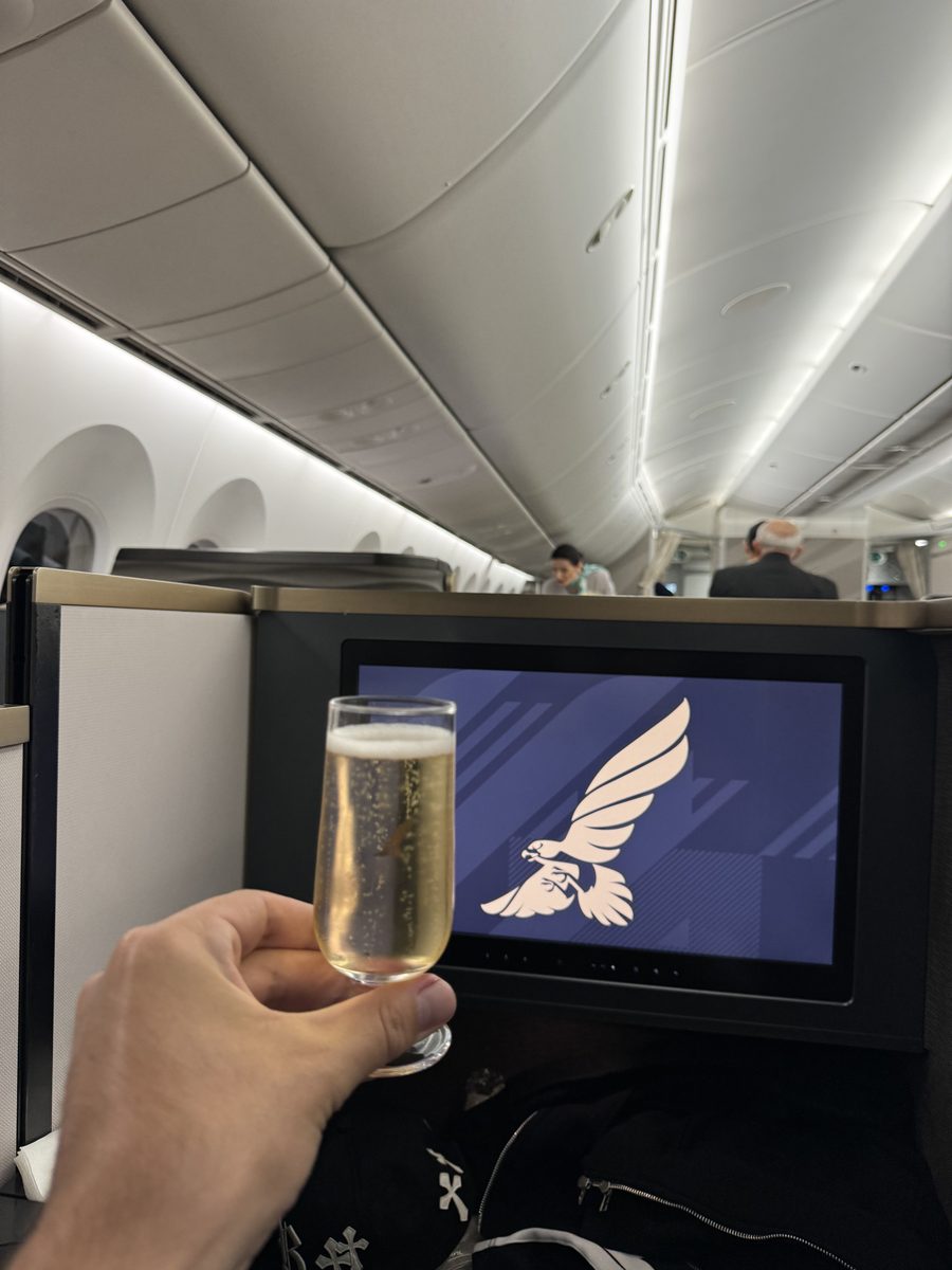 Coupe de champagne levée devant l'écran de la suite business Gulf Air affichant le faucon doré de la compagnie