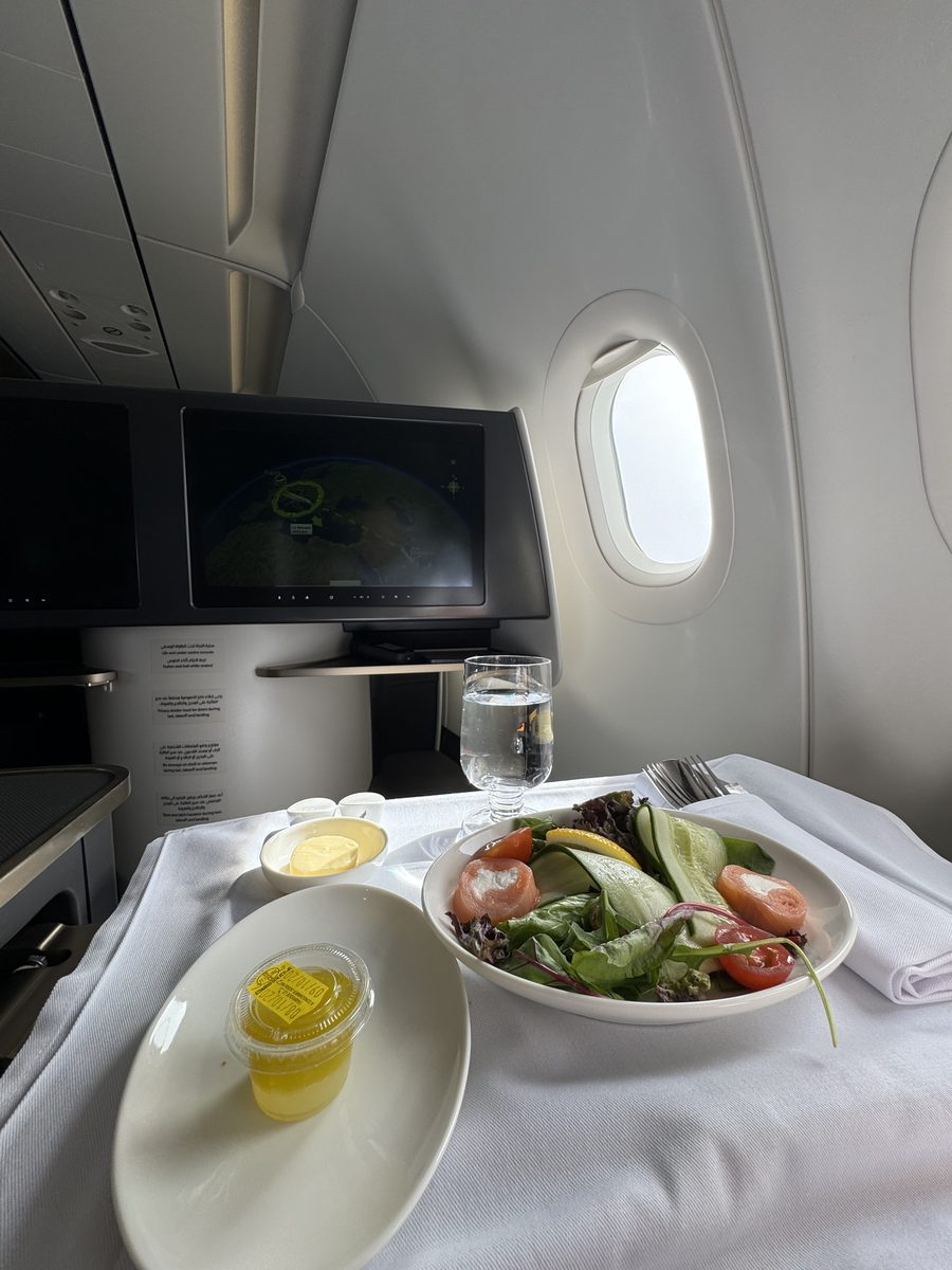Entrée de saumon et salade servie sur nappe blanche en business Gulf Air, avec la carte du vol Paris–Bahreïn à l'écran