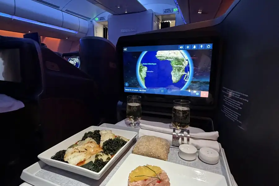 Plateau-repas gastronomique en classe affaires, écran de navigation affichant la carte de vol