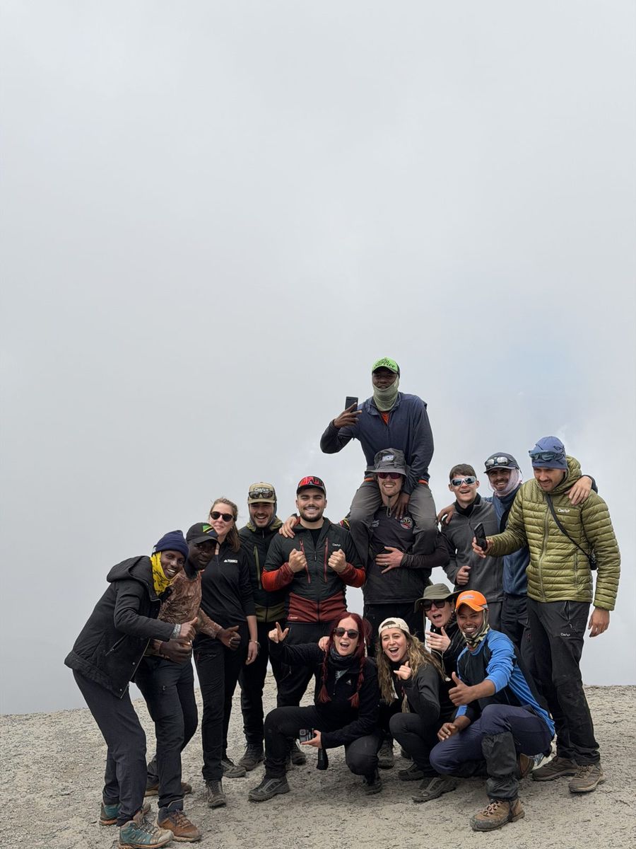 Groupe de trekkeurs souriants au sommet du Kilimandjaro dans la brume, portés sur les épaules