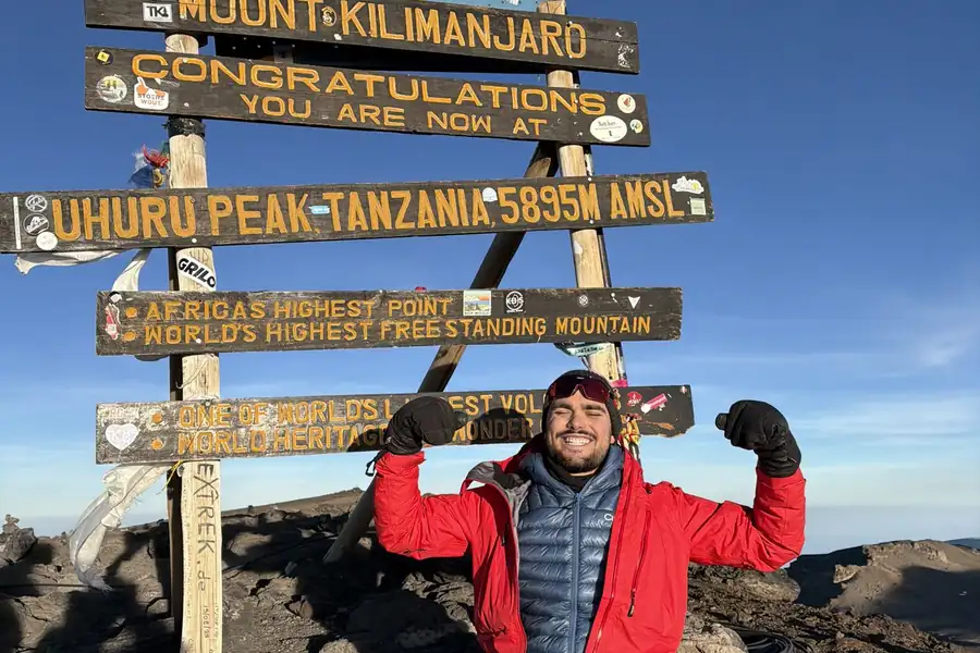 Lucas au sommet du Kilimandjaro devant le panneau Uhuru Peak, 5895m, bras levés en signe de victoire