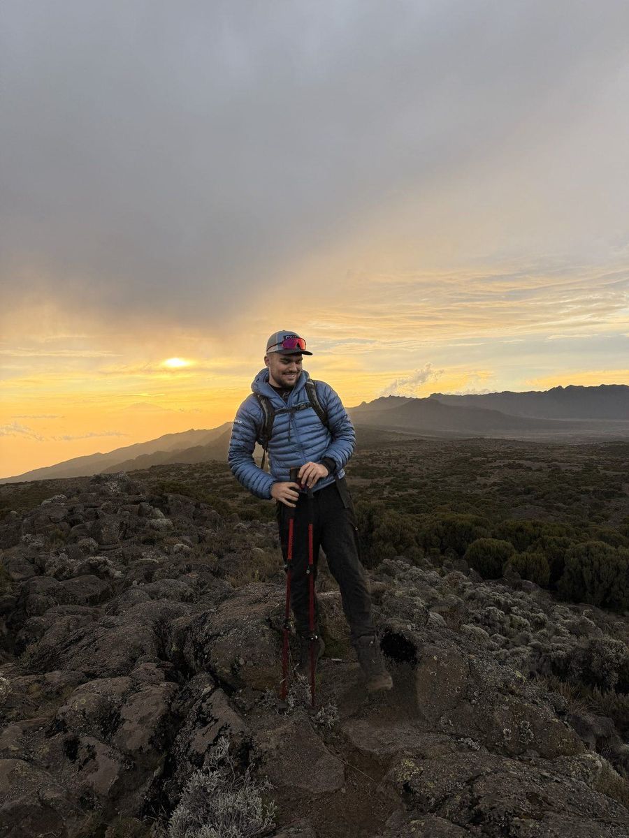 Lucas de profil sur un sentier volcanique du Kilimandjaro au coucher du soleil, bâtons de marche à la main