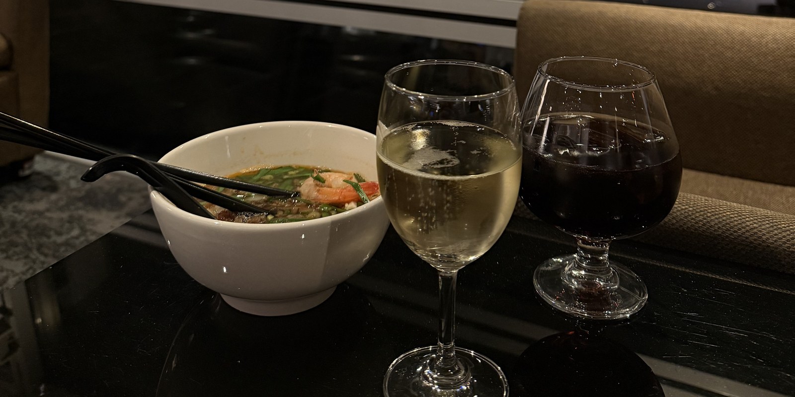 Plateau de nouilles et deux verres de vin au salon de l'aéroport de Kuala Lumpur, vue sur le tarmac de nuit