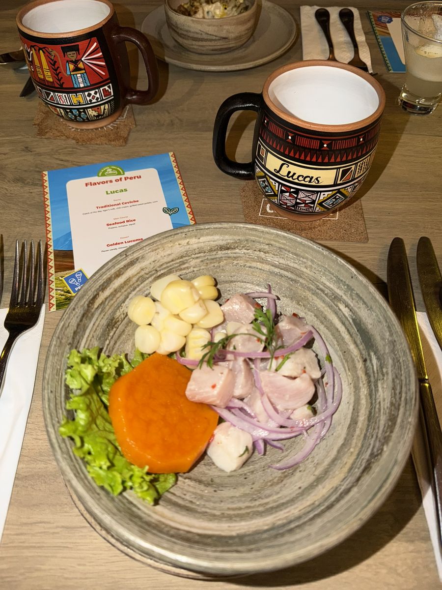 Assiette de ceviche traditionnel avec maïs géant, patate douce et oignons rouges, deux mugs en céramique péruvienne et un verre de pisco sour