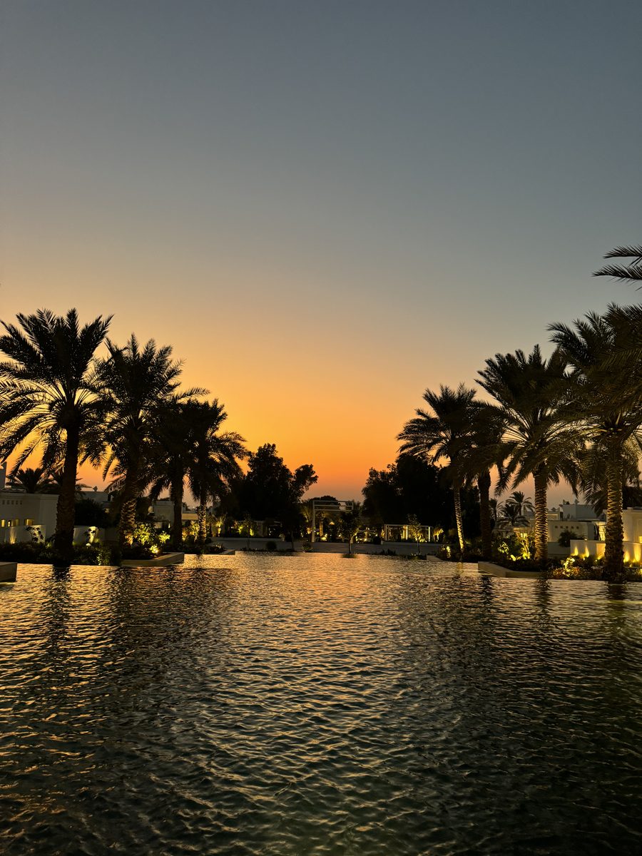 La grande piscine du Raffles Al Areen Palace Bahrain bordée de palmiers au coucher du soleil, ciel orange